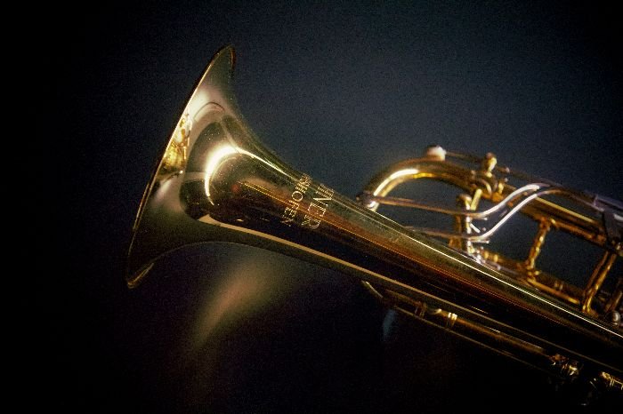 Close-up of a polished brass trumpet against a dark background, highlighting the gleaming metal surface and intricate details, exemplifying the result of a successful brass restoration process.