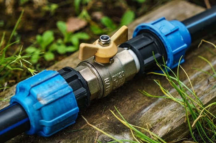 A close-up of a water pipe with a shut-off valve and blue pipe insulation, set against a natural backdrop, representing weatherizing techniques to prevent water damage in varying London weather conditions.