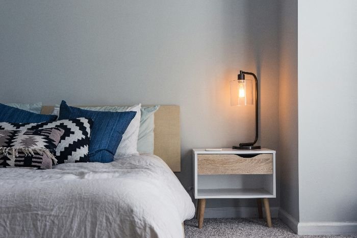 A tidy and well-kept bedroom corner, with a stylish lamp on a nightstand next to a cozy bed, showcasing a dust-free surface ideal for a deep cleaning process.