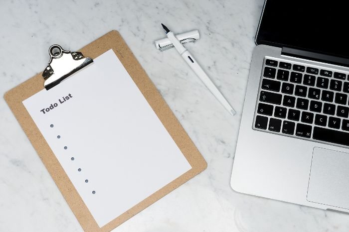 A blank to-do list on a clipboard with a pen, next to a laptop and a razor, symbolizing the planning and organisation of tasks.