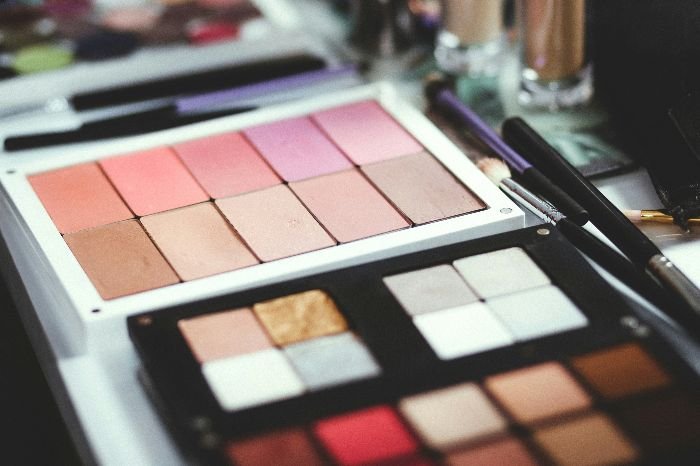 An open makeup palette with a range of blush, eyeshadow colors, and brushes, highlighting the products that can potentially cause stains on delicate fabrics if not handled properly.