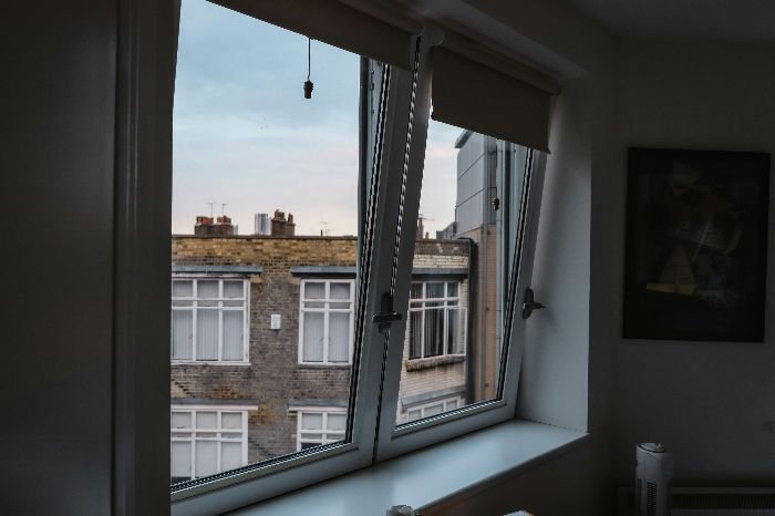 An open window in a city apartment with a view of neighboring buildings, letting in natural light and fresh air, ready for a thorough cleaning to ensure a streak-free finish for end-of-tenancy inspection.