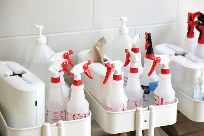 An assortment of labeled cleaning spray bottles neatly arranged in caddies, illustrating the need to understand and organize cleaning products for safe and effective use.