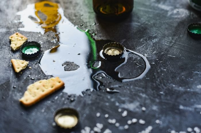 Aftermath of a party scene with spilled beverages, bottle caps, and crackers on a dark textured surface, illustrating the need for effective cleaning solutions.