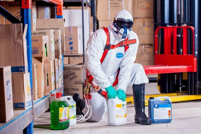 A professional cleaner in protective gear handling chemicals safely in a storage area, underscoring the critical importance of safe cleaning practices to avoid health risks.