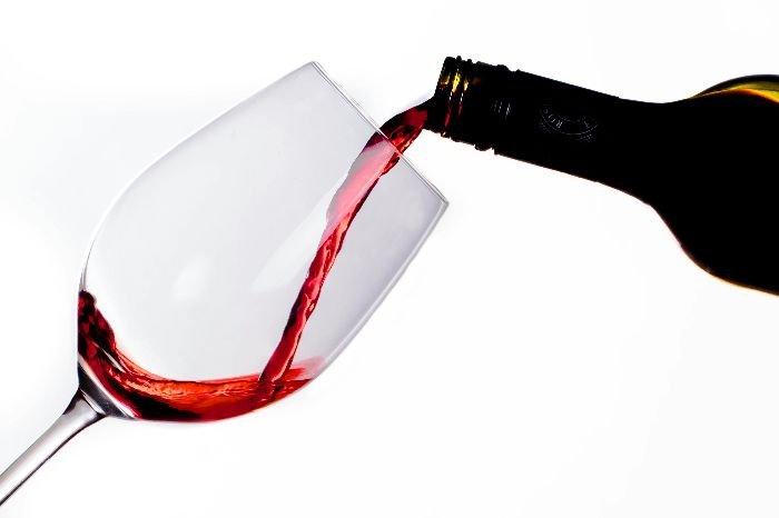 Red wine being poured into a tilted wine glass against a white background, demonstrating the potential for stains needing removal.