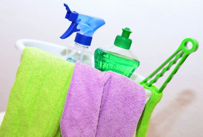 Cleaning supplies including a spray bottle, green soap, and colorful microfiber cloths on a white background, ready for a living room speed-clean.