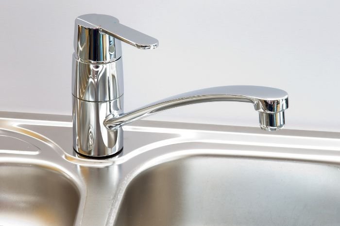 A shiny chrome kitchen faucet over a stainless steel sink, perfectly polished and free from limescale, illustrating the goal of limescale removal in home maintenance.