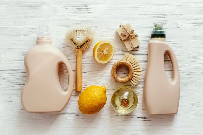 A neatly arranged set of eco-friendly cleaning tools including brushes, a lemon, and natural soaps, emphasizing the use of reusable and biodegradable products in household cleaning.