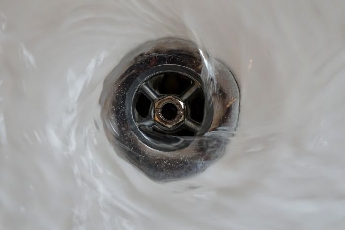 Water swirling down a drain where signs of limescale buildup are visible, highlighting the need for regular maintenance to prevent hard water deposits.