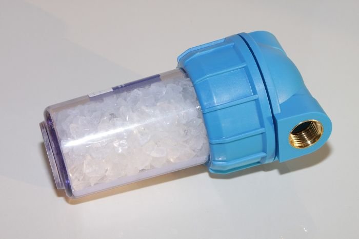 A close-up of a blue water softener filled with clear resin beads, illustrating a home water treatment solution designed to combat hard water and prevent limescale buildup.