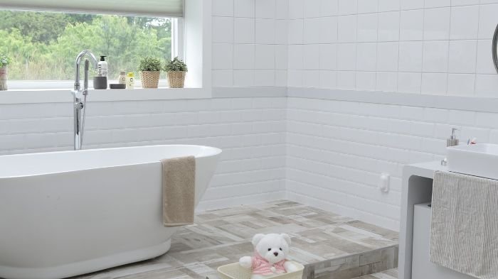 Spacious bathroom with a freestanding tub and a plush teddy bear on the floor, illustrating the importance of regular inspections for grout and silicone seal maintenance to preserve the room's pristine condition.