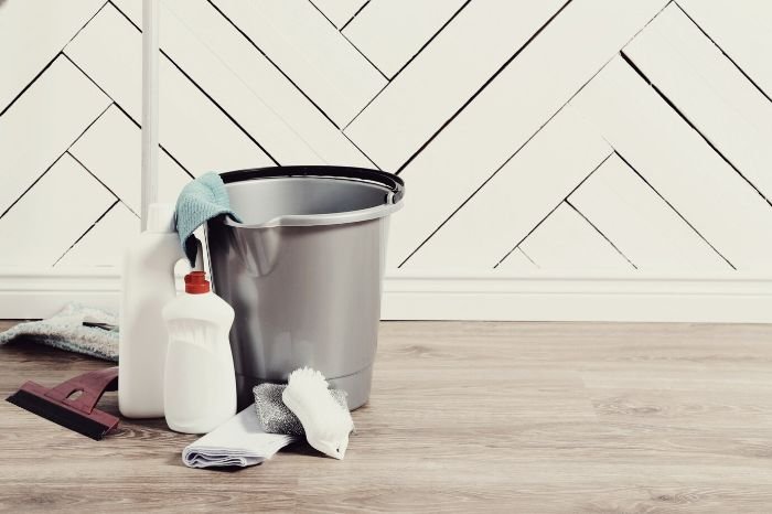 A bucket with essential cleaning supplies, including a stain remover, cloths, and gloves, prepared for effective home stain removal.