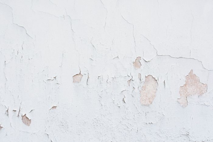 A close-up of a wall with peeling paint and visible cracks, underscoring the necessity for preventative measures against water damage.