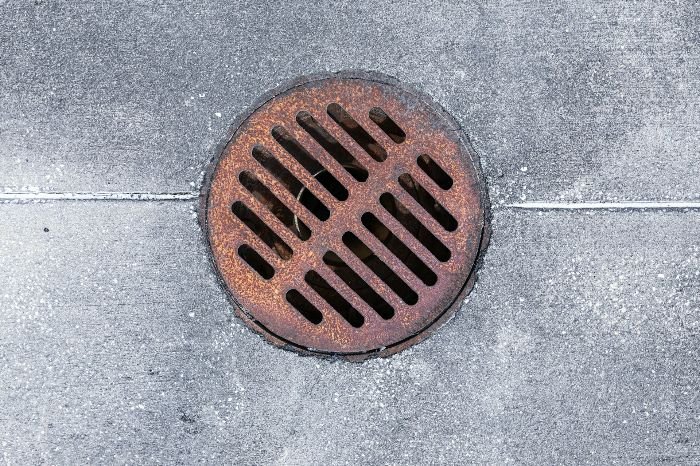 A rust-covered metal drain grate embedded in concrete, depicting the typical appearance of rust stains on metal surfaces.