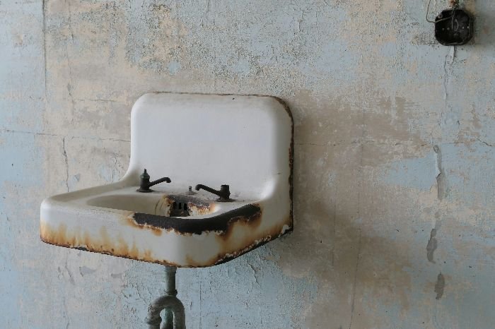 A corroded metal sink against a distressed wall, demonstrating the impact of rust and the need for careful treatment.