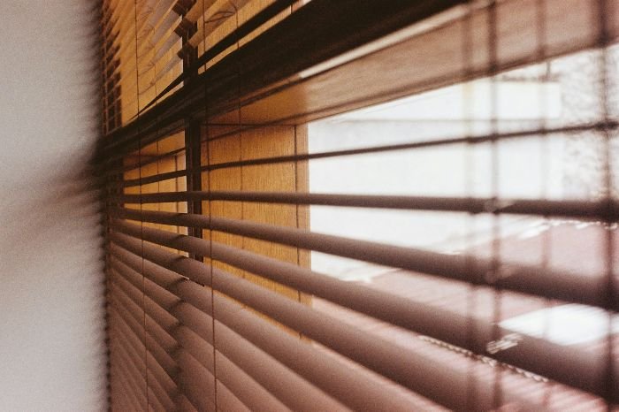 Warm sunlight filters through Venetian blinds, casting shadows on the wall, setting the perfect stage for discussing the simplicity of blind cleaning in different living spaces.