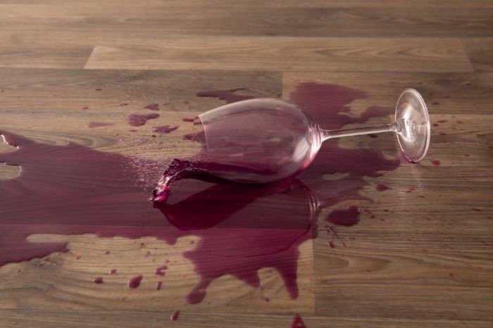 A tipped-over wine glass with red wine spilled across a wooden table, exemplifying the need for effective surfactants in stain removal.