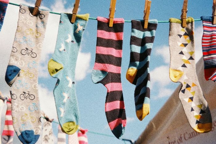 A row of quirky, patterned socks hanging on a clothesline against a clear blue sky, ready to be repurposed into handy dusting gloves for eco-friendly home cleaning.